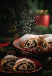 Icing sugar falls on poppy seed cake on red plate surrounded by Christmas decorations