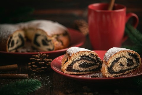 Poppy seed cake on a red plate surrounded by pine branches and a cup