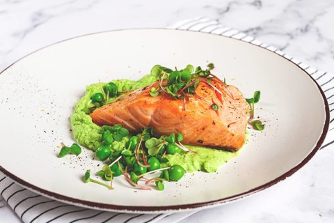 Delicious grilled salmon is placed elegantly on creamy green pea puree. Fresh microgreens and peas
