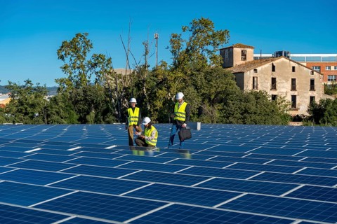Three engineers wearing safety helmets and vests performing an inspection of a large rooftop solar