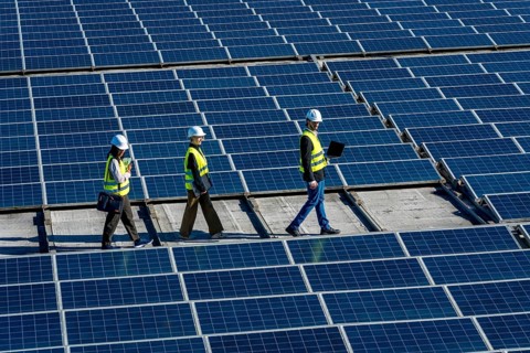 Three engineers walking on a rooftop solar power station, checking and inspecting the large array