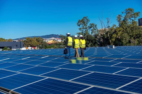 Team of engineers is inspecting an array of solar panels on a rooftop power plant, working on a