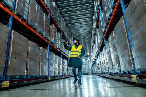 Worker in protective clothing and safety vest holding a barcode scanner, checking products in a