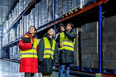 Diverse warehouse team in safety vests and warm protective gear scanning and checking inventory on