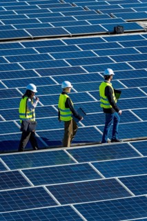 Engineers wearing safety vests and hard hats are walking across a vast array of solar panels at a