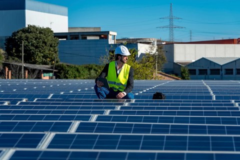 Engineer in a hard hat and high visibility vest inspecting solar panel rows on a large rooftop