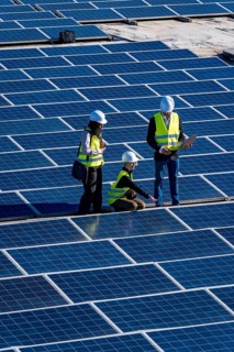 Engineers and technicians inspecting solar panels on a large solar farm, collaborating and