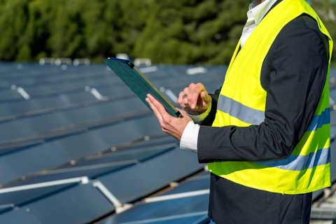 Engineer in safety vest and suit jacket holds clipboard and pen while inspecting and recording data