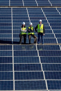 Team of diverse engineers with hard hats and safety vests standing confidently on a large solar