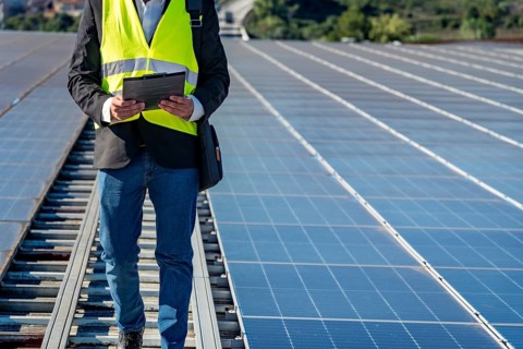 Technician working on a large solar panel installation, reviewing data on a clipboard while walking