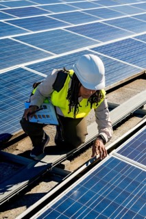 Woman engineer in a hard hat and safety vest inspecting solar panels on a rooftop, working on