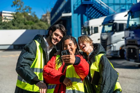 Group of smiling logistics workers wearing protective vests and warm jackets creating a cheerful