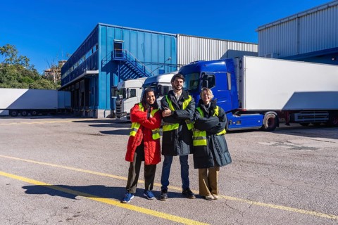 Logistics team members smiling, wearing safety vests and warm clothing, standing outdoors with arms