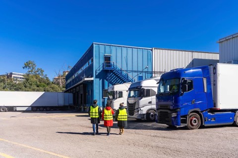 Logistics workers in high visibility vests walking past semi trucks parked at the loading docks of