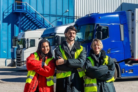 Diverse logistics team in high visibility vests and insulated jackets standing with arms crossed