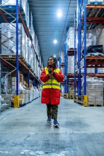 Woman wearing warm jacket and safety vest scanning inventory with a barcode reader, managing stock