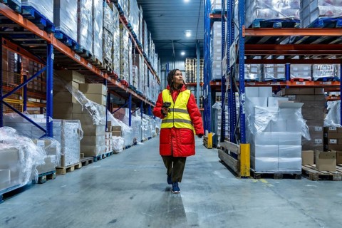 Female warehouse worker wearing warm clothing and a safety vest, scanning inventory while walking