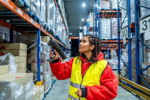 Worker wearing protective clothing and a high visibility vest scanning boxes on tall racks,