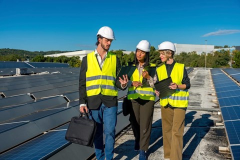 Team of diverse energy engineers and technicians inspecting solar panels on a rooftop, discussing