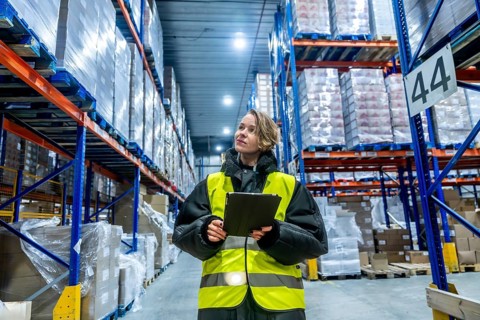 Woman worker wearing a warm jacket and high visibility vest using a digital tablet while checking