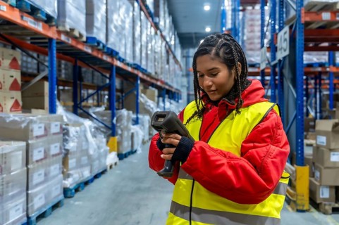 Logistics worker wearing warm clothing and a safety vest performing inventory checking with a