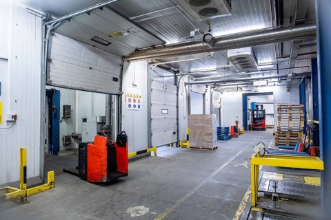 Industrial cold storage facility featuring multiple loading docks with pallet jacks and forklifts,