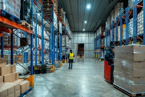 Workers are moving inventory using a forklift and inspecting goods on high racks in a large cold