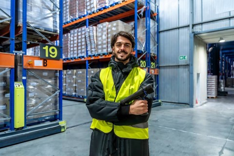 Man in safety vest and warm clothing holding a scanner, working in a cold storage warehouse with