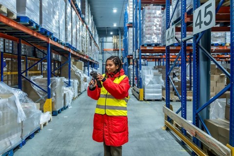 Woman worker in high visibility vest and warm jacket scanning pallets of boxes in a cold storage