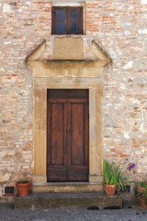Rustic wooden door in a brick façade with potted plants and a small window above, Tuscany, Italy
