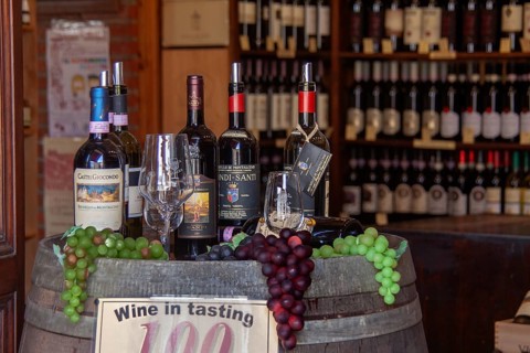 Cosy wine shop with wine bottles, glasses and grapes on a wooden barrel, Tuscany, Italy