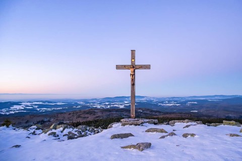 Christian cross on the peak of Mount Lusen with the view over the hills of the bavarian forest at