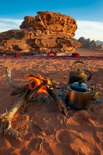 Two teapots next to an open fire in desert sand, eroded rocks in the background, Wadi Rum, Jordan
