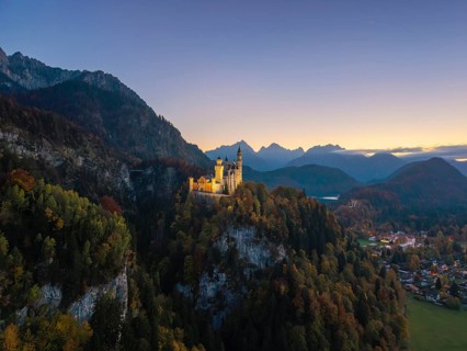 Charming Neuschwanstein Castle in evening light on a dense forest hill in front of impressive