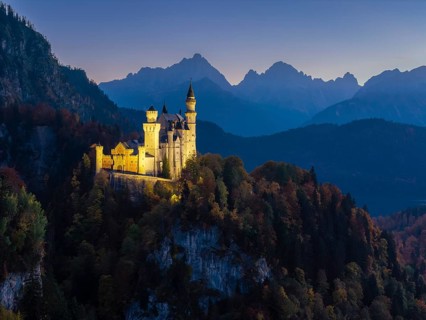 Sublime illuminated Neuschwanstein Castle on a ridge in the midst of an alpine landscape at sunset,