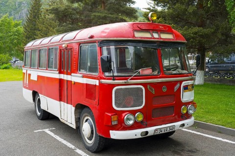 Red retro bus in a parking lot surrounded by trees and green nature, PAZ-672, minibus from Soviet