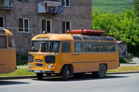 A vintage bus in orange with roof luggage, parked on a street against a green background, PAZ-672,