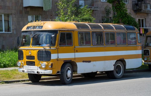 An old retro bus in orange parked on a street next to a building, PAZ-672, minibus from the Soviet