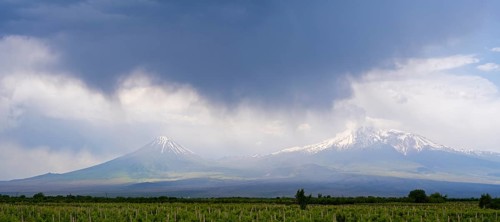 Two snow-capped mountains under dramatic skies with dark clouds over vast fields, Ararat and Little