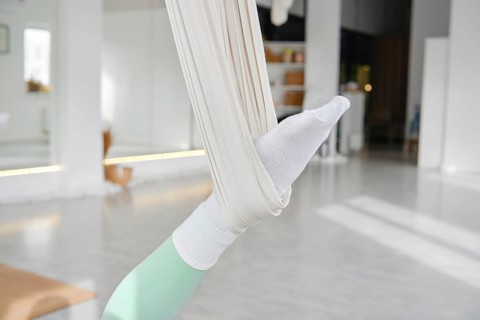 A person engages in fitness stretching using a hammock for support. The scene is set in a bright