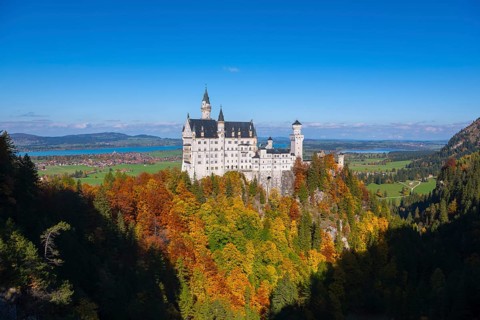 The magnificent Neuschwanstein Castle surrounded by autumn colors and vast green hills, Schwangau,