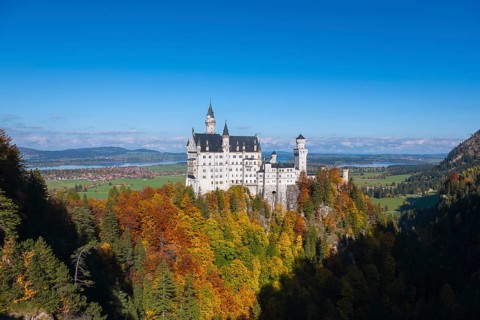 The majestic Neuschwanstein Castle rises above colorful autumn trees against a blue sky, Schwangau,