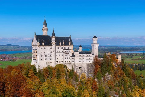 Impressive Neuschwanstein Castle in autumn landscape, surrounded by colorful trees and under blue