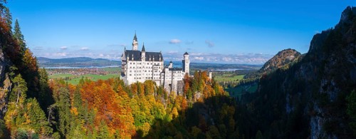 Neuschwanstein Castle towers over colorful forests in a vast landscape with blue skies, Schwangau,