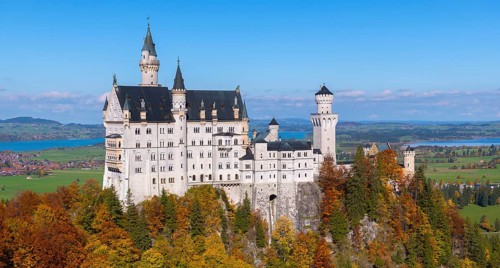 A detailed view of Neuschwanstein Castle with autumn colors and wide fields in the background,