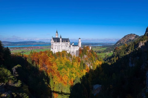 The impressive Neuschwanstein Castle surrounded by colorful autumn trees and a vast landscape,