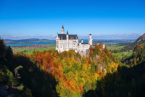 The impressive Neuschwanstein Castle in front of a vast autumn landscape with bright blue sky,