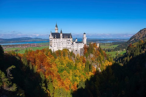 The magnificent Neuschwanstein Castle towers over an autumnal landscape with wide skies, Schwangau,