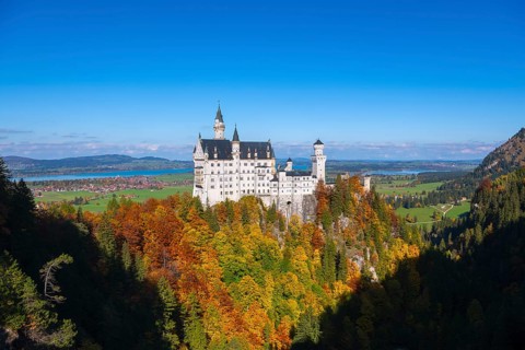 The picturesque Neuschwanstein Castle overlooks colorful autumn forests under clear skies,