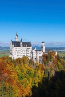 Neuschwanstein Castle stands majestically above colorful autumn forests and bright blue skies,